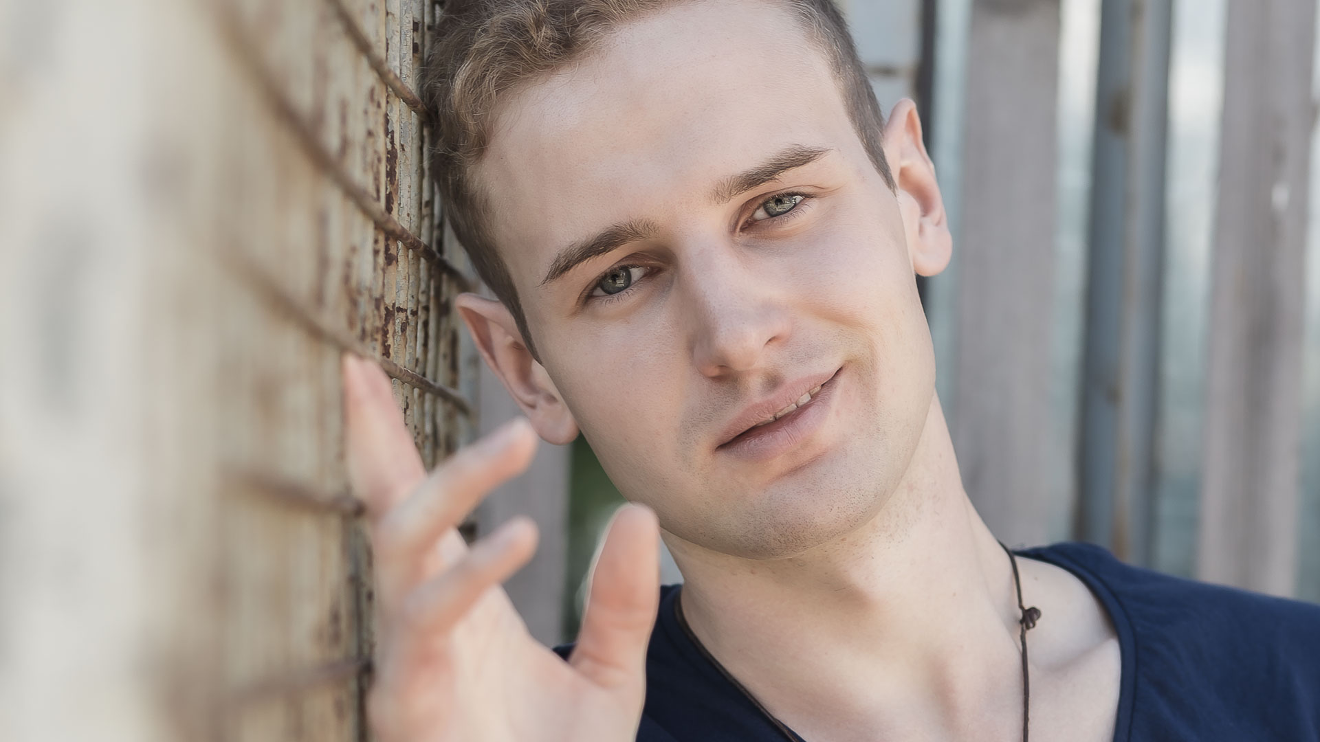 Tinder-Foto eines junges Mannes, der an einer Wand angehent sich und sympathisch lächelt.