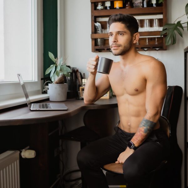 Home Shooting-Mann, Mann mit nackten Oberkörper sitzt am Schreibtisch und trinkt einen Kaffee