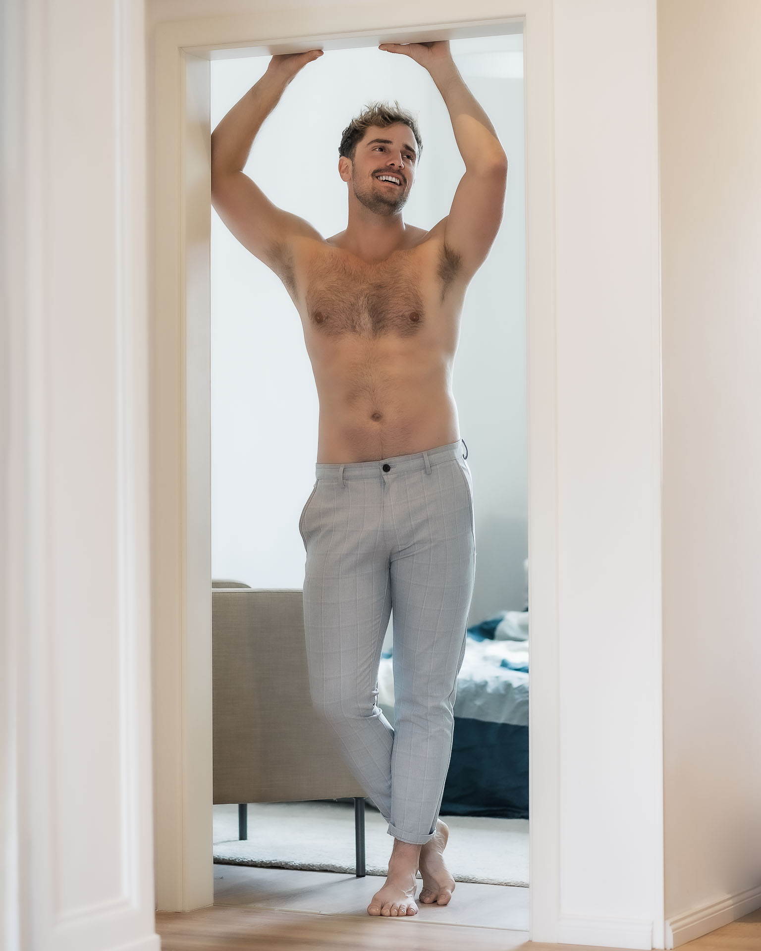 Ein attraktiver Mann steht oberköperfrei in seiner Wohnung im Türrahmen